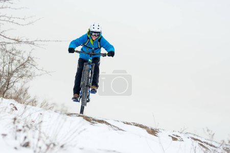 Foto de Ciclista en azul descansando con bicicleta de montaña en la colina rocosa de invierno. Concepto de deporte extremo y ciclismo enduro. - Imagen libre de derechos