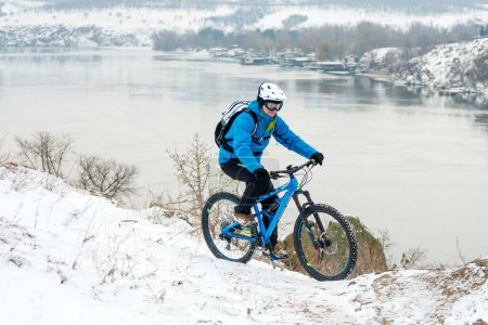 Foto de Ciclista en azul descansando con bicicleta de montaña en la colina rocosa de invierno. Concepto de deporte extremo y ciclismo enduro. - Imagen libre de derechos
