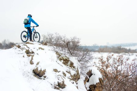 Photo for Cyclist in blue resting with mountain bike on rocky winter hill. Extreme sport and enduro biking concept. - Royalty Free Image