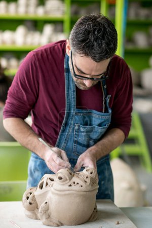 Photo for Portrait of ceramist dressed in an apron working on clay sculpture in bright ceramic workshop. - Royalty Free Image