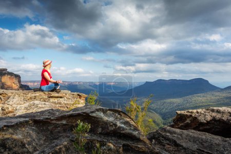 Téléchargez les photos : Jeune femme assise sur le bord du rocher avec belle vue sur la montagne - en image libre de droit