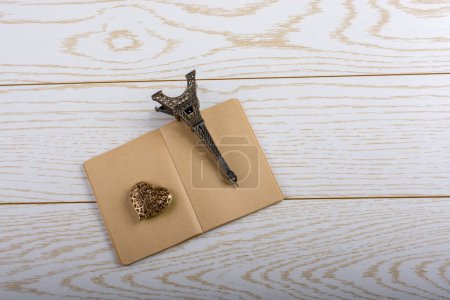 Photo for "Eiffel tower miniature and a steel heart on a brown notebook on " - Royalty Free Image