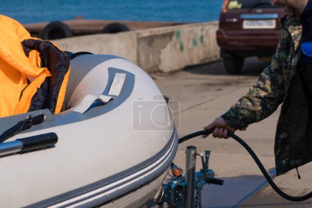 Téléchargez les photos : "Un homme lave un canot en caoutchouc après être allé en mer. Des gouttes d'eau se dispersent du bateau." - en image libre de droit