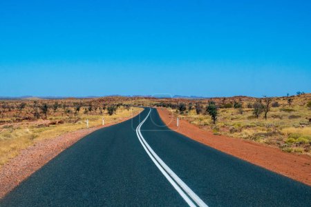 Photo for "Empty dark road leading through red sanded Australian landscape towards Karijini National Park" - Royalty Free Image