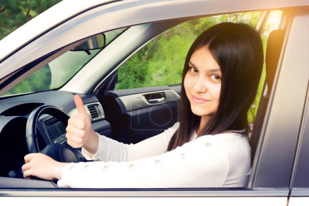 Photo for Happy young girl with long dark hair driving a car and gesturing thumb up - Royalty Free Image