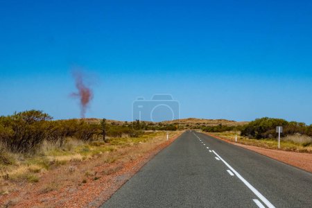 Photo for "Dust devil besides dark road leading through red sanded Australian landscape towards Karijini National Park" - Royalty Free Image