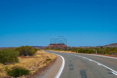 Photo for "Hill behind empty road in Western Australia leading towards Karijini National Park" - Royalty Free Image