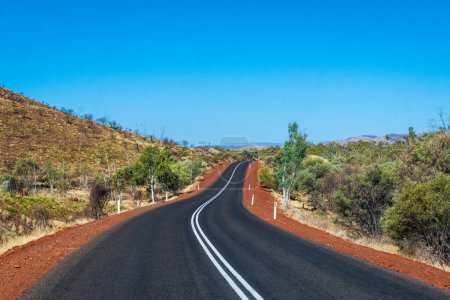 "Route avec tarmac sombre menant entre les collines au parc national de Karijini Australie"