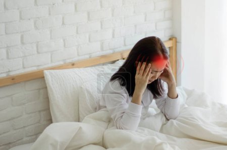 Foto de Una mujer sentada en la cama con dolor de cabeza - Imagen libre de derechos