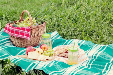 Foto de Picnic en la hierba en un día de verano - cesta, uvas, queso, pan, manzanas - un concepto de recreación al aire libre de verano - Imagen libre de derechos