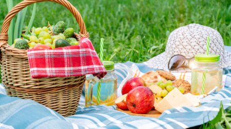 Téléchargez les photos : Pique-nique sur l'herbe un jour d'été - panier, raisin, fromage, pain, pommes - un concept de loisirs d'été en plein air - en image libre de droit