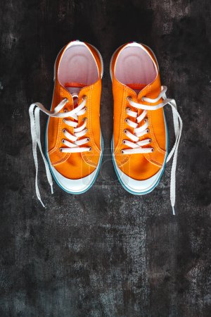 Téléchargez les photos : Baskets jaune-orange avec lacets détachés sur un fond en béton foncé - en image libre de droit
