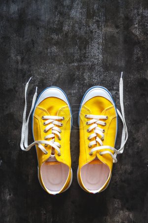 Téléchargez les photos : Baskets jaune-orange avec lacets détachés sur un fond en béton foncé - en image libre de droit