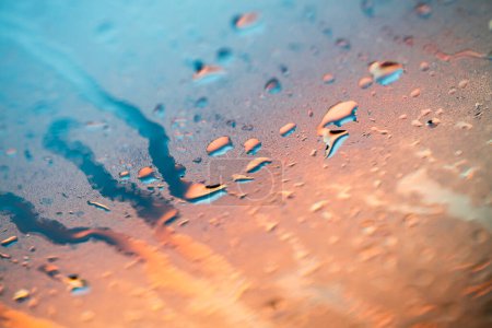 Photo for Closeup through window of rainy day with water dripping down glass against blurred colorful background - Royalty Free Image