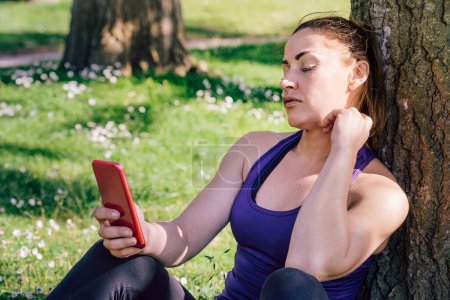 Photo for Sports woman looking at her phone while resting - Royalty Free Image