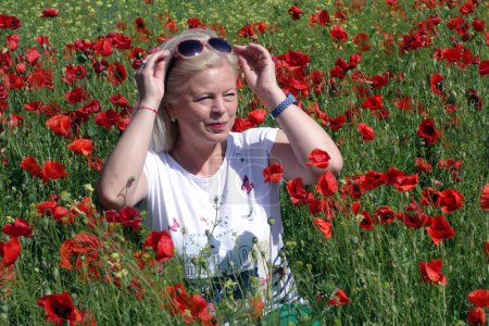 Téléchargez les photos : A blond woman smiling at the field full of poppies - en image libre de droit