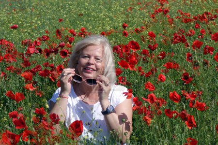 Téléchargez les photos : Une femme blonde souriant au champ plein de coquelicots - en image libre de droit