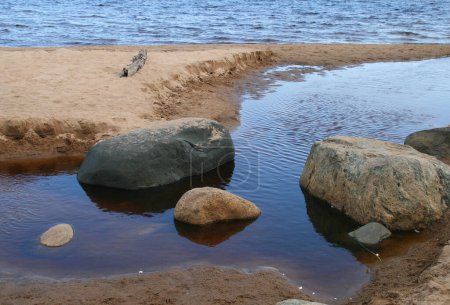 Foto de Grandes piedras en la orilla de un lago azul con un banco de arena. - Imagen libre de derechos