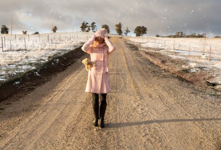 Photo for "Happy go lucky woman walking down dirt road in light snow fall" - Royalty Free Image