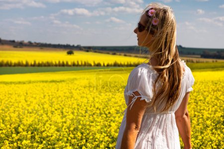 Téléchargez les photos : Femme en robe blanche debout près des champs de canola doré - en image libre de droit
