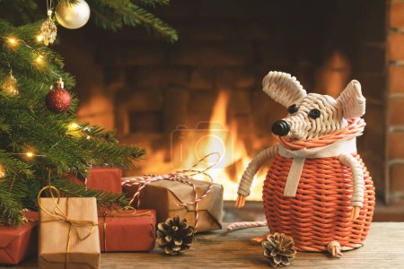 Téléchargez les photos : Composition de Noël - une souris blanche en osier - symbole de 2020 selon l'horoscope chinois à côté de cadeaux sous l'arbre de Noël dans la chambre par cheminée - en image libre de droit