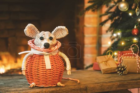 Téléchargez les photos : Composition de Noël - une souris blanche en osier - symbole de 2020 selon l'horoscope chinois à côté de cadeaux sous l'arbre de Noël dans la chambre par cheminée - en image libre de droit