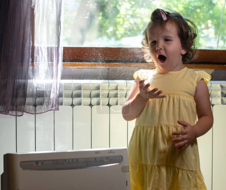 Photo for Little girl in a dusty room. Air purifier and coughing kid. Dust - Royalty Free Image