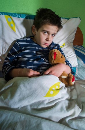 Téléchargez les photos : Enfant malade au lit avec ours en peluche - en image libre de droit