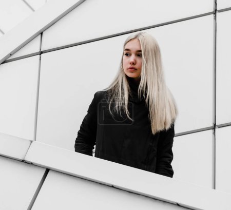 Photo for Young girl with blond hair and black clothes against a gray building - Royalty Free Image