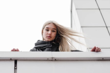 Téléchargez les photos : Jeune fille aux cheveux blonds et vêtements noirs contre un bâtiment gris - en image libre de droit