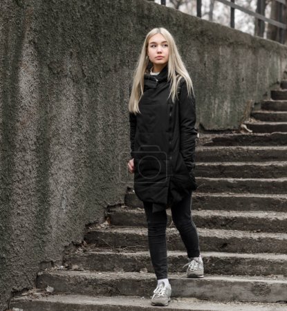 Téléchargez les photos : Jeune fille aux cheveux blonds en vêtements noirs descend les escaliers en pierre - en image libre de droit