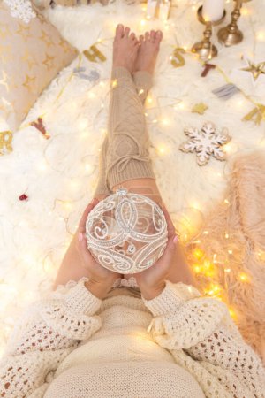 Foto de La hembra sostiene un adorno reluciente entre las decoraciones de Navidad - Imagen libre de derechos
