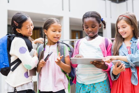 Téléchargez les photos : Enfants utilisant une tablette numérique et un téléphone portable sur la terrasse de l'école - en image libre de droit