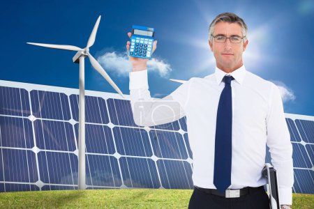 Téléchargez les photos : Homme d'affaires en costume tenant calculatrice contre des panneaux d'énergie verte - en image libre de droit