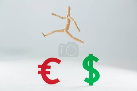 Photo for Wooden figurine jumping over dollar and euro symbols - Royalty Free Image