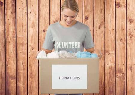 Photo for Happy volunteer looking at donation box against wooden background - Royalty Free Image