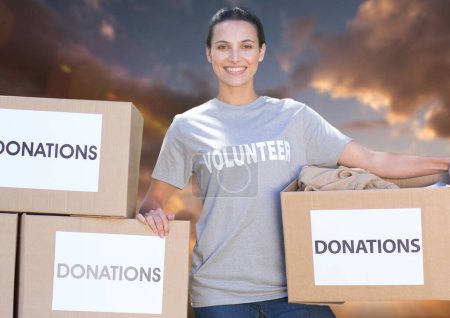 Photo for Smiling volunteer with donation box against sky background - Royalty Free Image