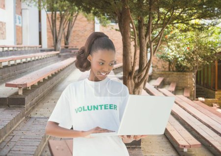 Foto de Voluntario sonriente usando la computadora contra el fondo del campus - Imagen libre de derechos