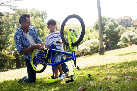 Photo for Son and father repairing their bicycle in park - Royalty Free Image