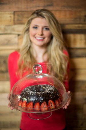 Photo for Portrait of smiling woman holding a cake stand with chocolate cake - Royalty Free Image