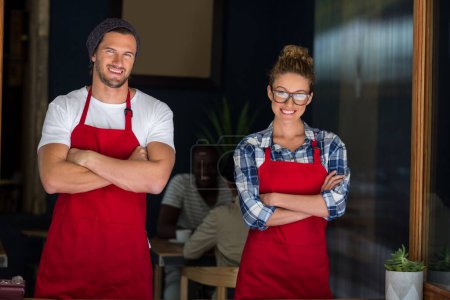 Photo for Smiling waitress and waiter standing with arms crossed outside cafe - Royalty Free Image