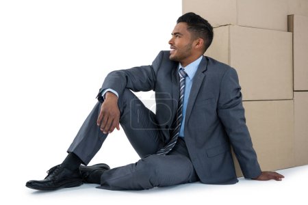 Photo for Businessman sitting near cardboard boxes against white background - Royalty Free Image