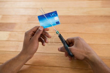 Foto de Empresario cortando tarjeta de crédito con tijeras sobre fondo de madera - Imagen libre de derechos