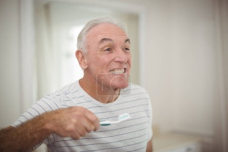 Téléchargez les photos : Portrait d'un homme âgé tenant une brosse à dents dans sa salle de bain - en image libre de droit