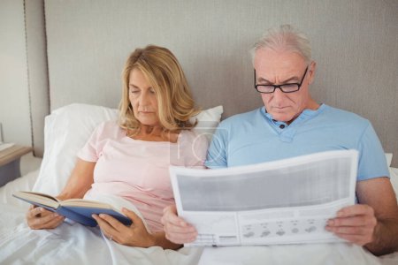 Téléchargez les photos : "Couple aîné sur le lit lire le journal et le livre
" - en image libre de droit