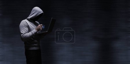 Photo for Composite image of hacker using laptop while holding credit card - Royalty Free Image