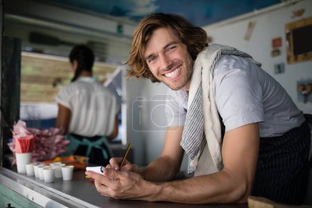 Photo for Portrait of waiter writing in notepad at counter - Royalty Free Image
