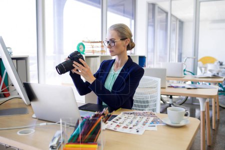 Téléchargez les photos : Femme cadre examinant une photographie prise à son bureau - en image libre de droit
