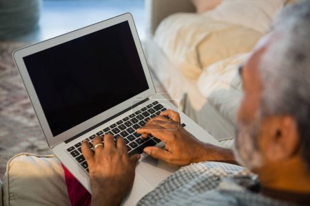 Téléchargez les photos : Homme âgé utilisant un ordinateur portable dans le salon - en image libre de droit