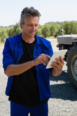 Téléchargez les photos : Travailleur utilisant une tablette numérique sur la route par une journée ensoleillée - en image libre de droit
